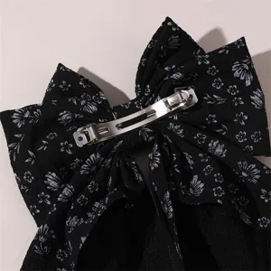 Close-up detail of the black floral fabric bow hair clip, showing the back spring clip.