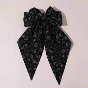 Close-up detail of black floral fabric hair bow clip with long ribbons, sweet style.