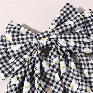 Close up detail of a black and white gingham bow hair clip featuring cute daisy embroidery.