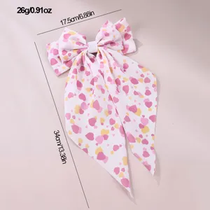 Bow hair clip detail view showing pink heart print fabric and long ribbon streamers.