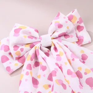 Close-up detail of a sweet pink heart print fabric bow hair clip with long ribbons.