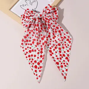 Close-up detail shot of a sweet red and white floral print fabric bow hair clip with streamers.