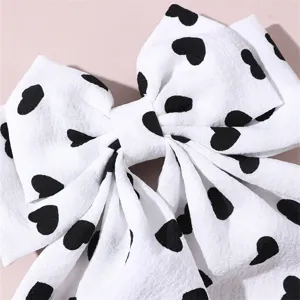 Close-up detail of white fabric hair bow clip featuring cute black heart pattern print.