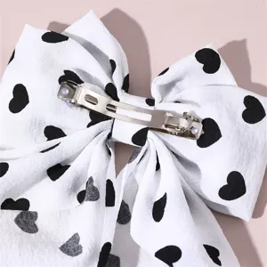 Detailed closeup of a white fabric hair bow with black hearts and metal spring clip.