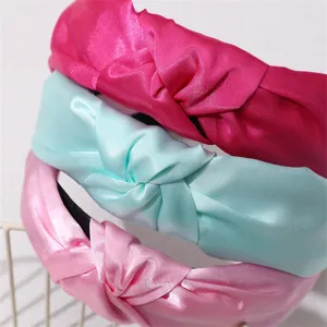 Close-up detail of three stacked satin knotted headbands in vibrant pink, mint and light pink.