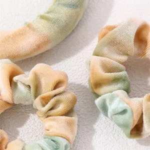 Close-up detail of tie-dye velvet hair scrunchies in green and orange gradient colors.