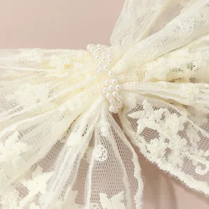 Close-up view of a white lace bow hair clip showing delicate mesh texture and pearl center.