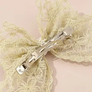 Gold lace bow hair clip detail showing durable metal spring barrette and pearl accent decor