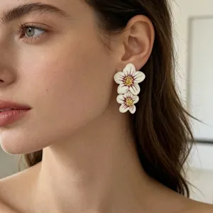 Gros plan detail des boucles dorees fleur email double couche portees sur les oreilles.