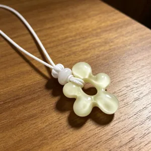 Pendentif fleur en résine gros plan, cordon tressé blanc, bijou style vacances vue de détail.