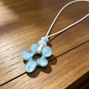 Gros plan d'un collier pendentif fleur en résine bleu clair avec cordon tressé sur surface en bois.