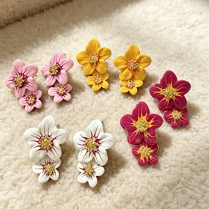 Détail de boucles d'oreilles clous fleurs en émail coloré à double pétale et pistils brillants.