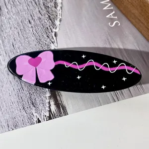 Primer plano detallado de la pinza de pelo ovalada negra con lazo rosa y detalles.