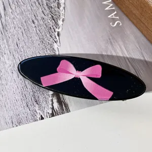 Primer plano de una horquilla ovalada negra con lazo rosa, accesorio de pelo bonito.