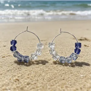 Gedetailleerd uitzicht van handgemaakte blauw-witte kristal kralen oorbellen op het strand.