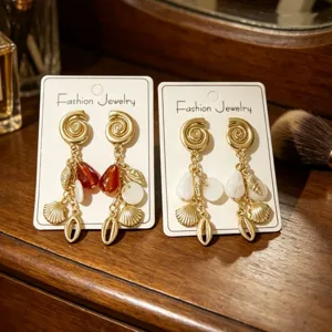 Primer plano de pendientes de borla de concha dorada en tarjetas, estilo de verano.