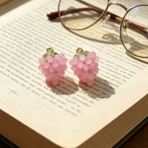 Gros plan des boucles d'oreilles raisin rose sur un livre ouvert avec un design délicat.