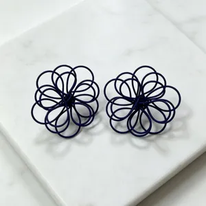 Closeup of dark blue woven wire flower earrings, detailed handmade petal design on white marble.