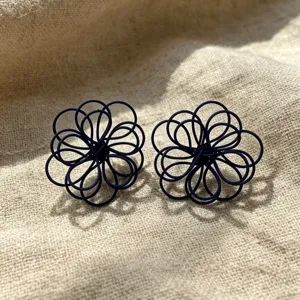 Close-up detail of dark blue woven wire flower stud earrings on textured linen background.