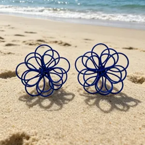 Detailed shot of blue wire-woven flower earrings displayed on a sunny beach sand backdrop.