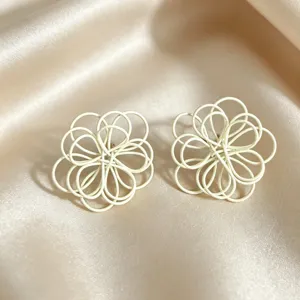 Close-up detail of white woven wire flower stud earrings on smooth silk background.