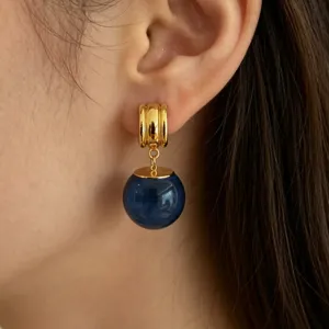 Gros plan détaillé de boucles d'oreilles créoles dorées avec pendentif sphère bleue.