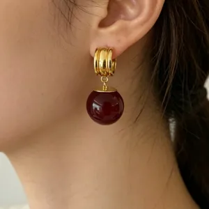 Gros plan détaillé de boucles d'oreilles créoles dorées avec pendentif perle rouge style.