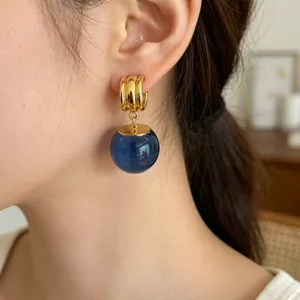 Gros plan de boucles d'oreilles créoles dorées avec un pendentif sphère en cristal bleu.