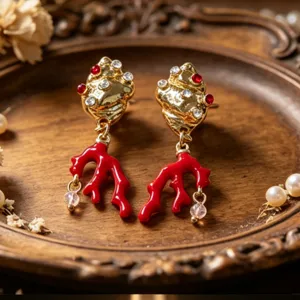 Detailopname van gouden schelp oorbellen met rode koraal en kristallen op houten dienblad.