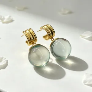 Gros plan des boucles d'oreilles créoles dorées en cristal vert, style rêveur.