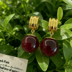 Gros plan de boucles d'oreilles vintage françaises créoles dorées et perles rouges sur fond de feuilles.