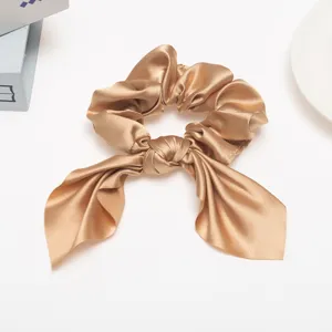 Detailed close-up shot of the elegant champagne satin hair scrunchie with a ribbon bow tail.