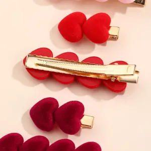 Close-up detail of red velvet heart hair clips with gold duckbill clips, soft texture.