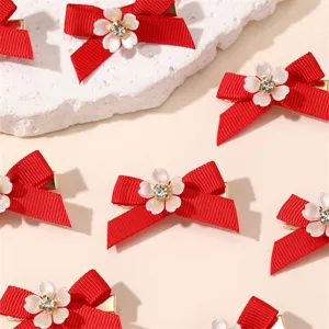 Detail shot of red bow hair clip with white floral rhinestone center, elegant festive accessory.