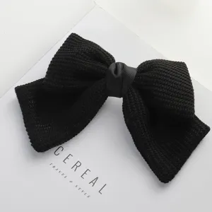 Detail view of a chic black knitted bow hair clip, featuring elegant ribbon center and secure spring clasp.