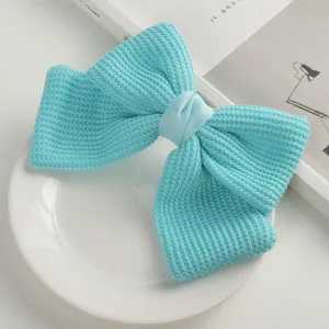 Cute knitted bow hair clip in vibrant turquoise color, elegant hair accessory for women detail shot.