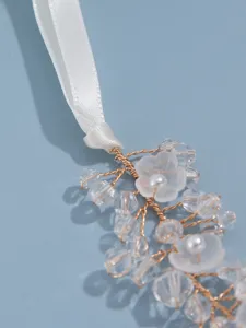 Close-up of bridal crystal flower hair accessory with white ribbon, gold wire, and pearl details.