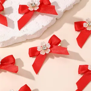 Red bow hair clip detail shot, featuring sparkling rhinestone and white flower accent for women.