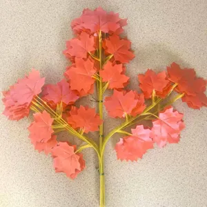 Detailed close-up view of artificial red maple leaf branch, showing realistic plastic foliage.
