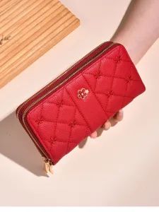 Detailed view of red quilted long wallet with floral charm, zipper closure and fine stitching.