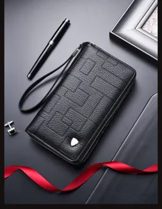 Detalle de billetera larga para hombre en cuero negro, con cremallera doble y correa de muñeca útil.
