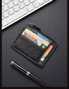 Close-up of black leather card holder with zipper pocket, multi-card slots, textured desk detail.