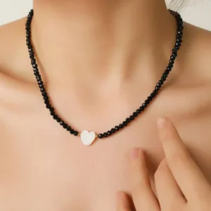 Collana girocollo di perline nere con ciondolo a cuore bianco, gioiello minimalista elegante.