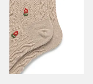 Close up of beige cable knit cotton socks with cute red floral embroidery details.