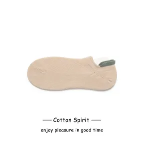 Primo piano di fantasmini in cotone beige a taglio basso con dettaglio del tacco verde a contrasto.