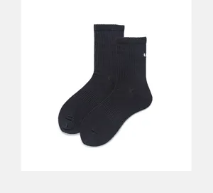 Close-up detail of black ribbed cotton crew socks with small white embroidered letter logo accent.