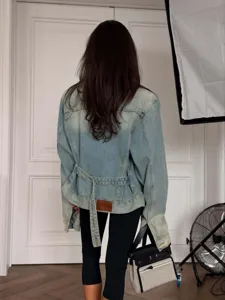 Back detail of vintage washed denim jacket with waist belt and leather patch for women.