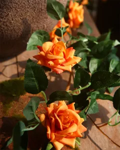 Close-up detail of artificial orange rose vine with lush green leaves for wall decor.