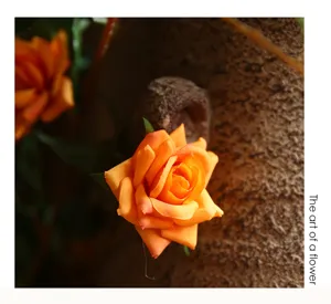 Detailed closeup of artificial orange rose flower with green leaf and textured vine stem.