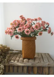 Artificial pink sunflower flower arrangement in woven vase for home decor tabletop detail view.